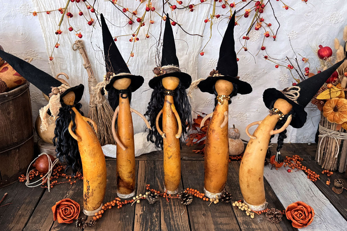 Five primitive gourd witches standing in various poses, each wearing a tall pointed black hat, handmade from natural gourds.