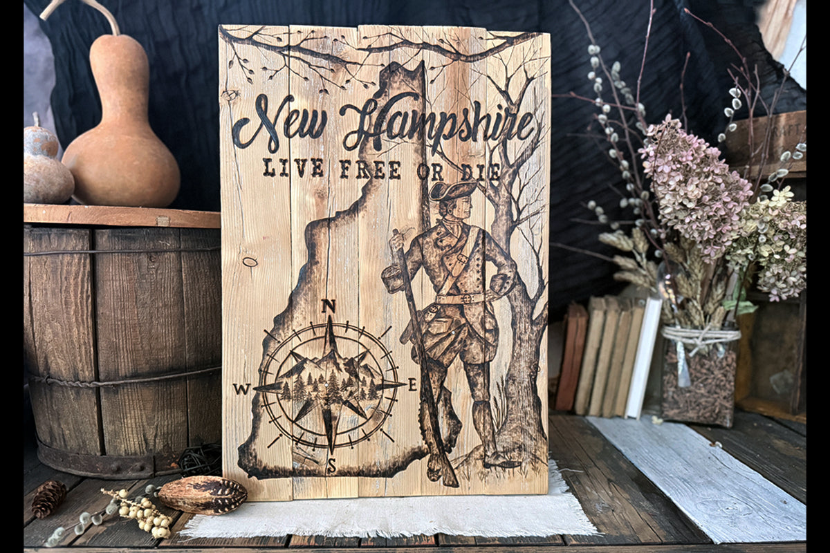 Handcrafted rustic wood wall art featuring a hand-burned map of New Hampshire with the White Mountains, a compass rose, a Colonial Revolutionary War soldier, and the motto 'Live Free or Die,' made from reclaimed pallet wood.