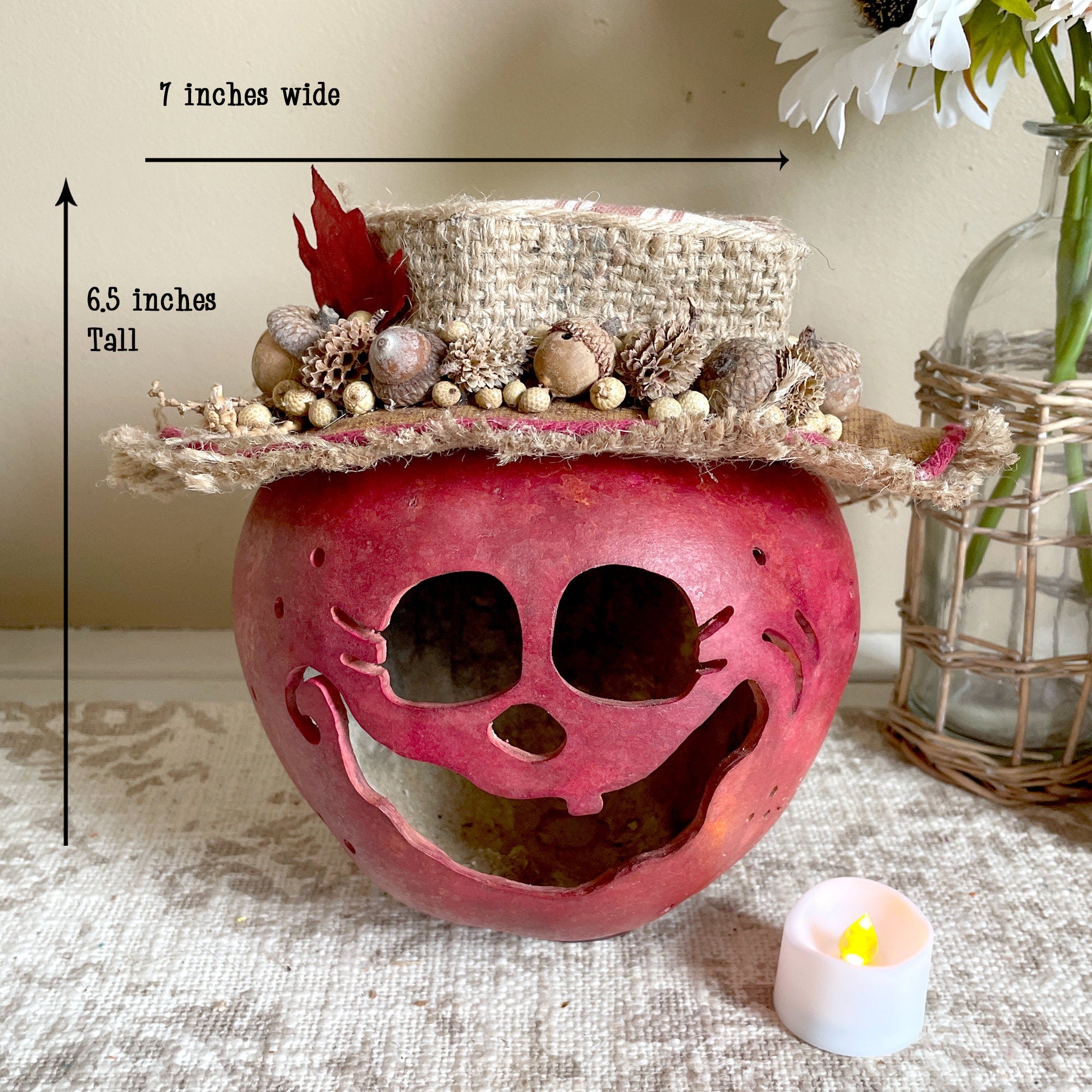 Decorative pink skull with straw hat on a textured surface, with measurements and a candle.
