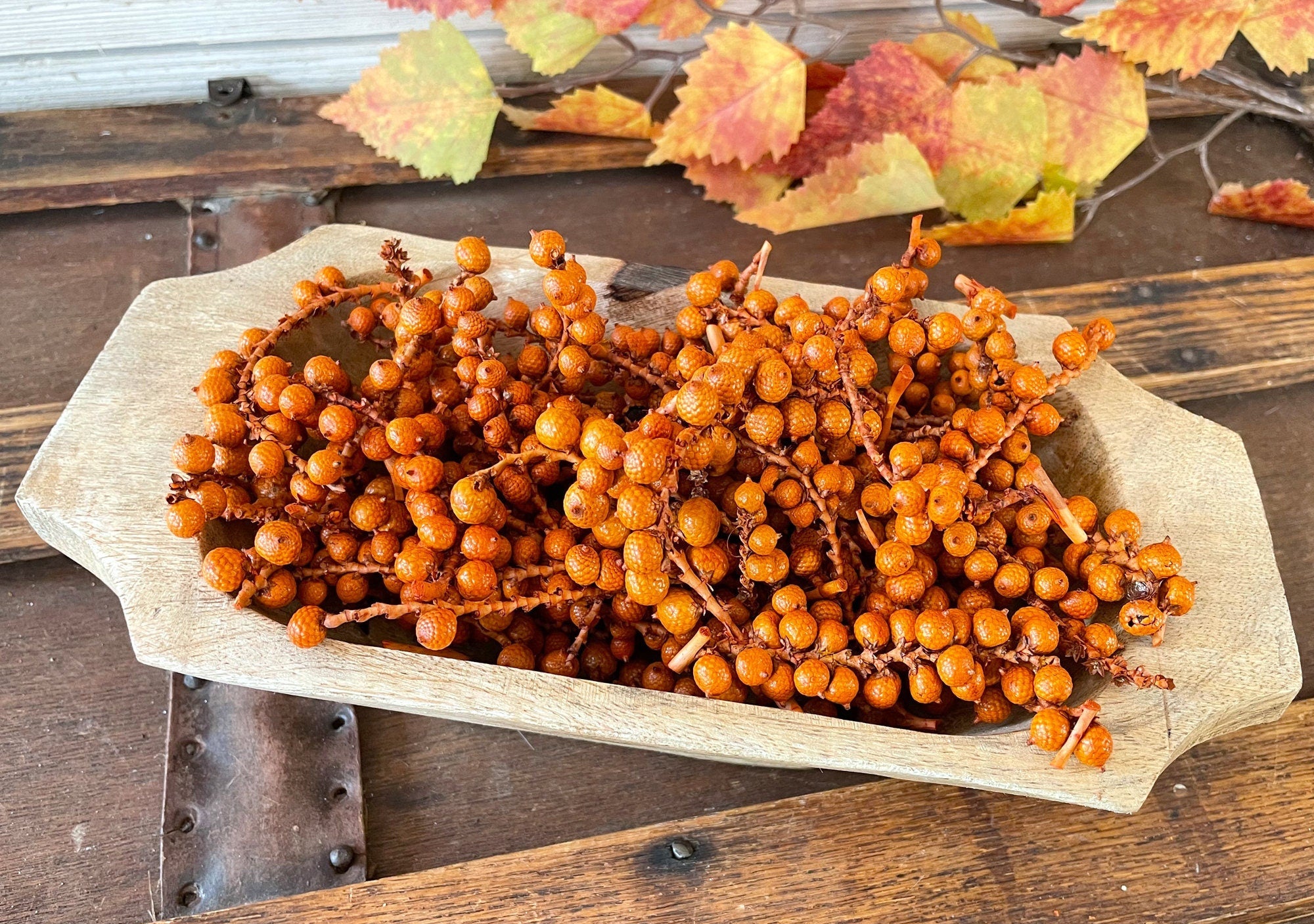 Bowl of orange berries on a wooden surface with autumn leaves