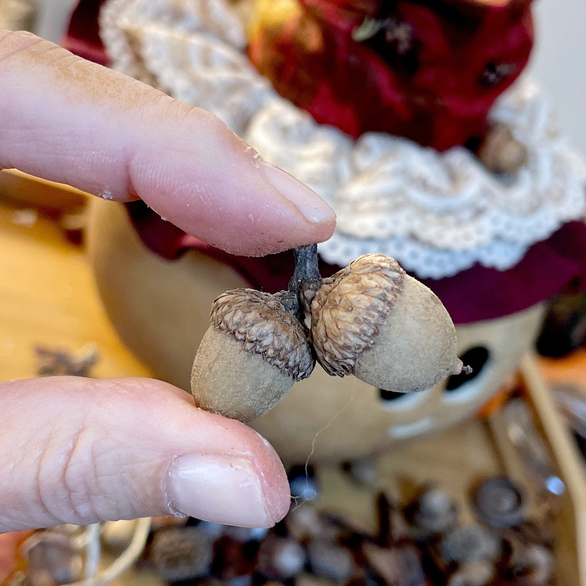 Hand holding two acorns with a blurred background of autumn decorations.