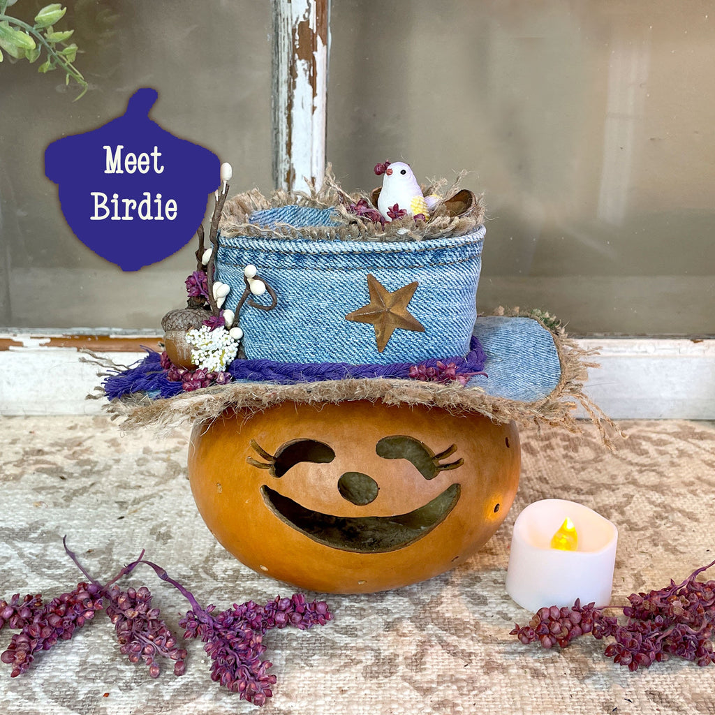 Decorative pumpkin with a face, blue basket, and small bird on a rustic surface with a candle.