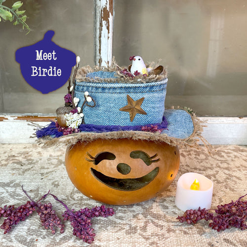 Decorative pumpkin with a face, blue basket, and small bird on a rustic surface with a candle.