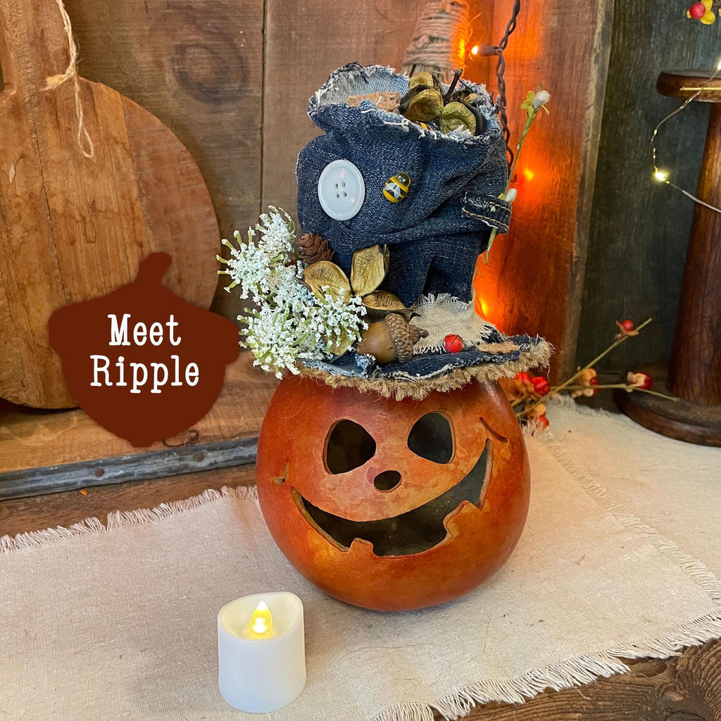 Decorative pumpkin with a small plush toy on top, surrounded by autumnal elements.