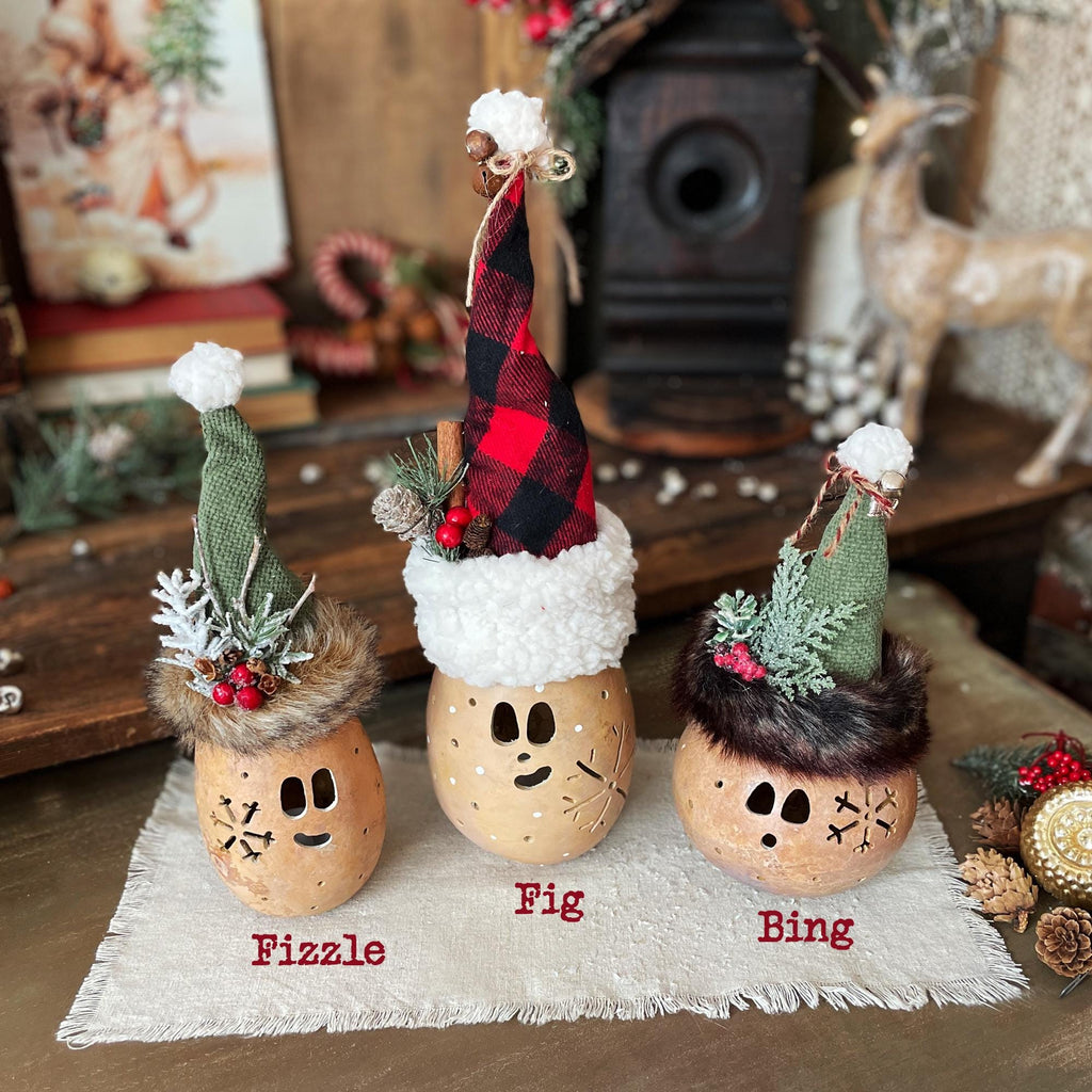 Three decorative holiday figures with names on a wooden surface.