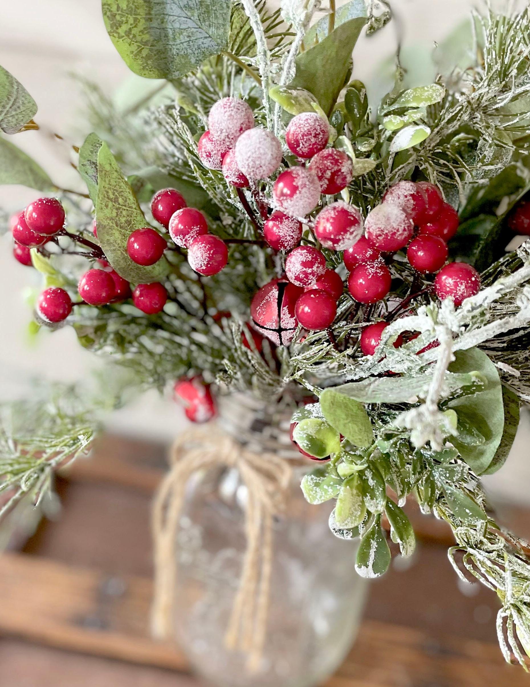 Decorative arrangement of red berries and greenery in a clear glass jar with a wooden lid.