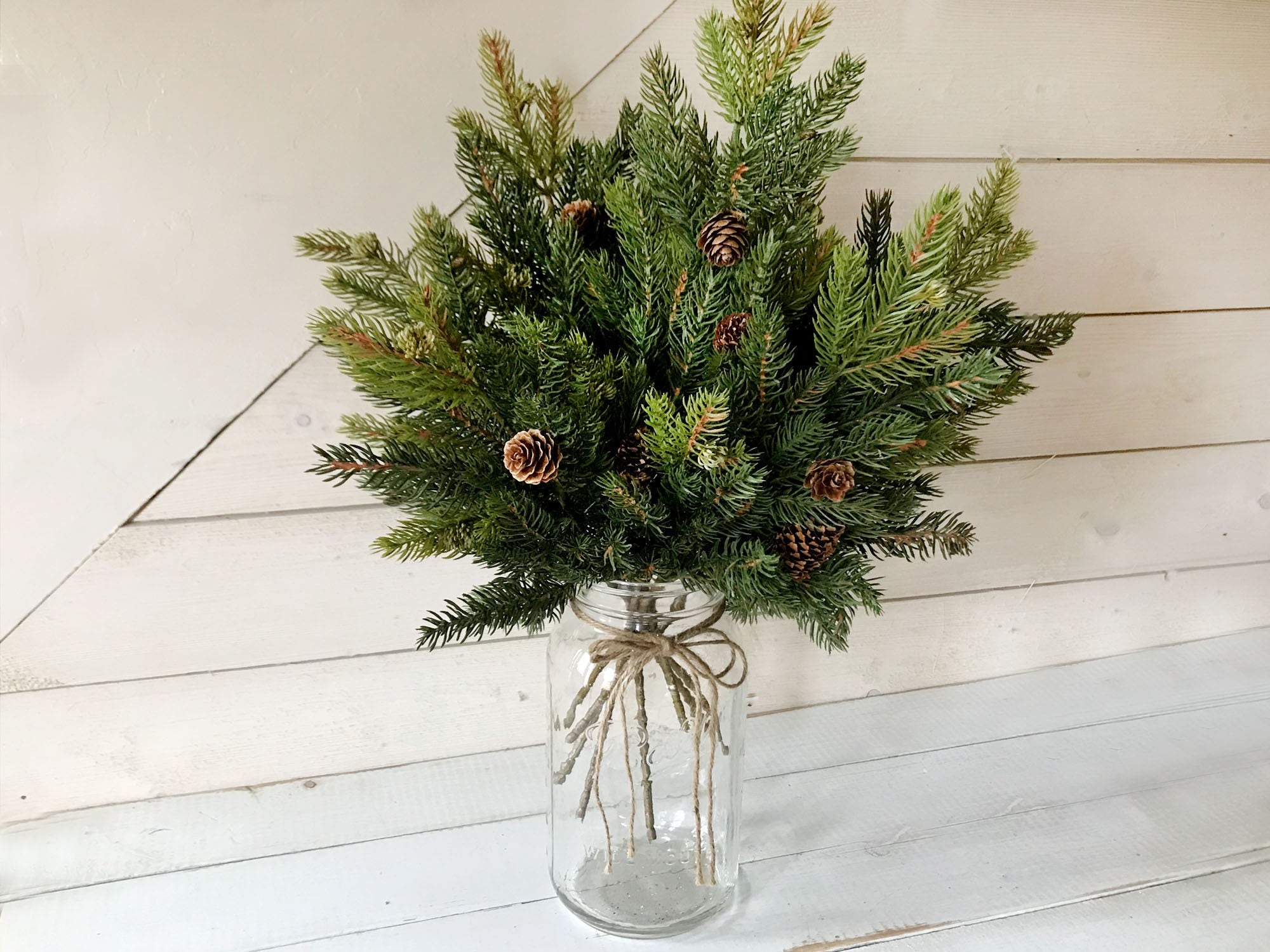 Bouquet of Fraser fur greenery in a glass jar with a white wooden background