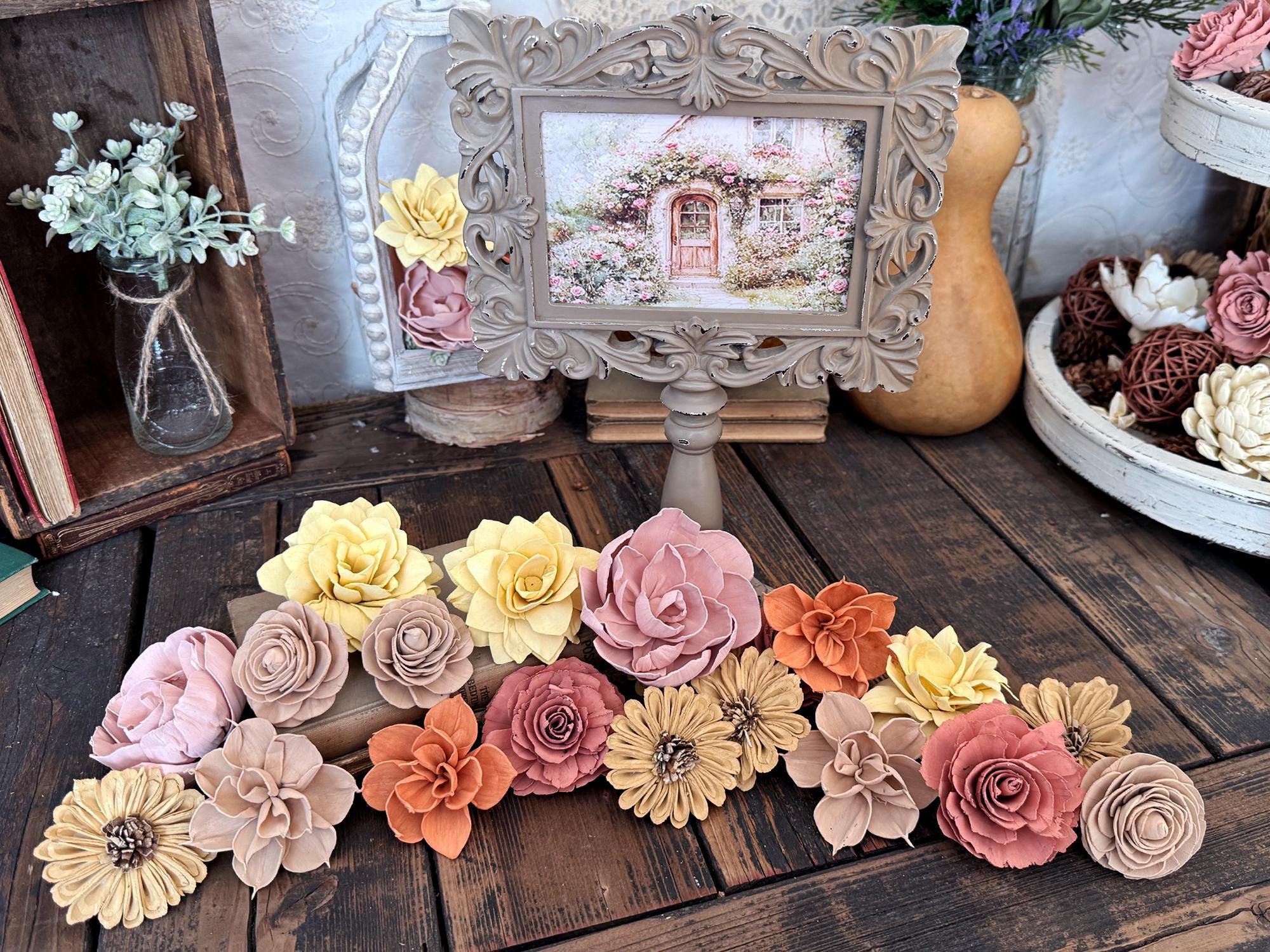 Decorative wood flowers arranged on a wooden surface with a framed picture in the background.