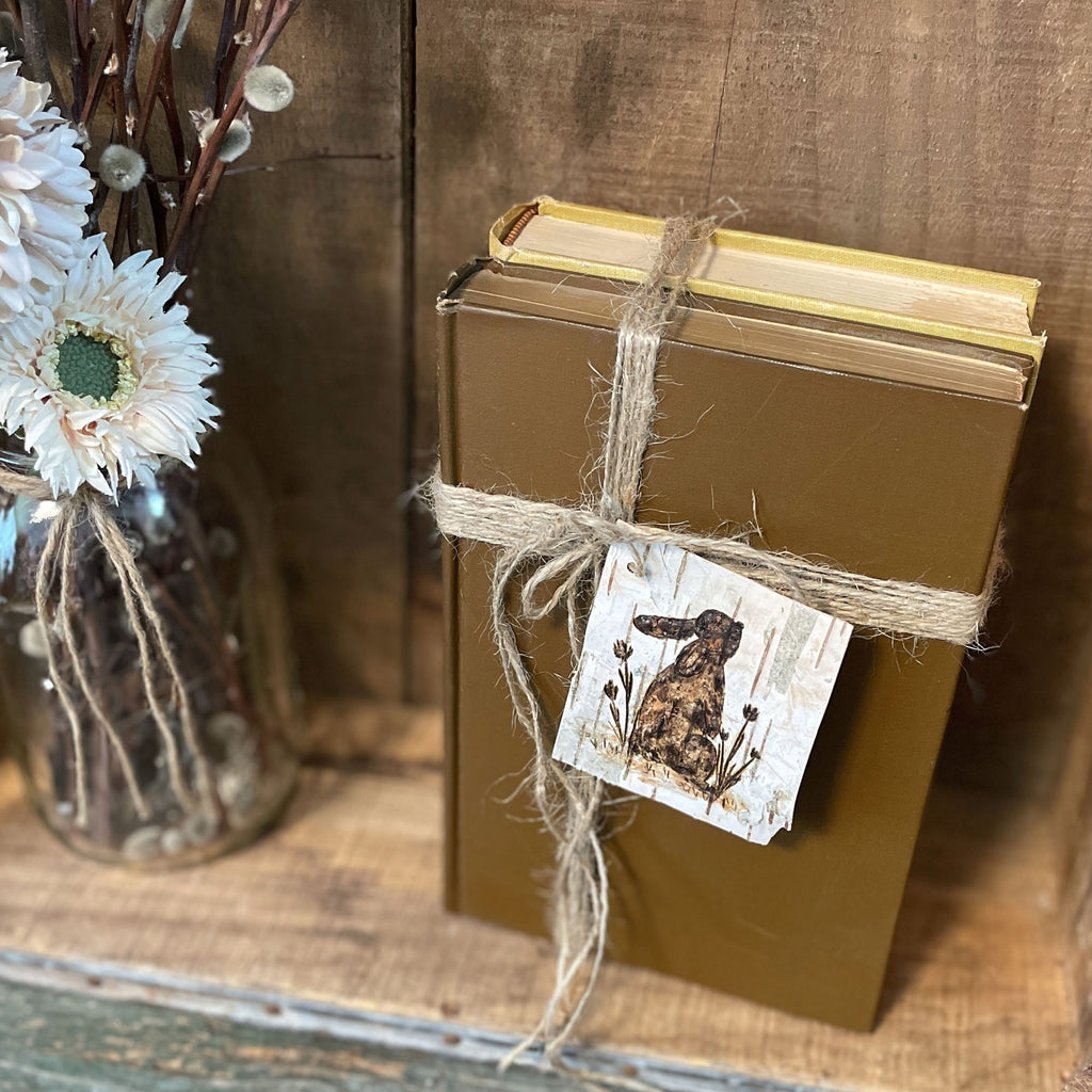 Brown book tied with twine and a decorative birch tag on a wooden surface with flowers in the background