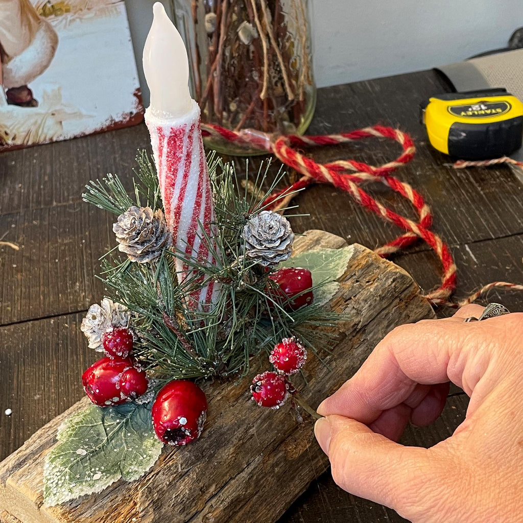Decorative setup with candles, pine cones, and berries on a wooden surface.