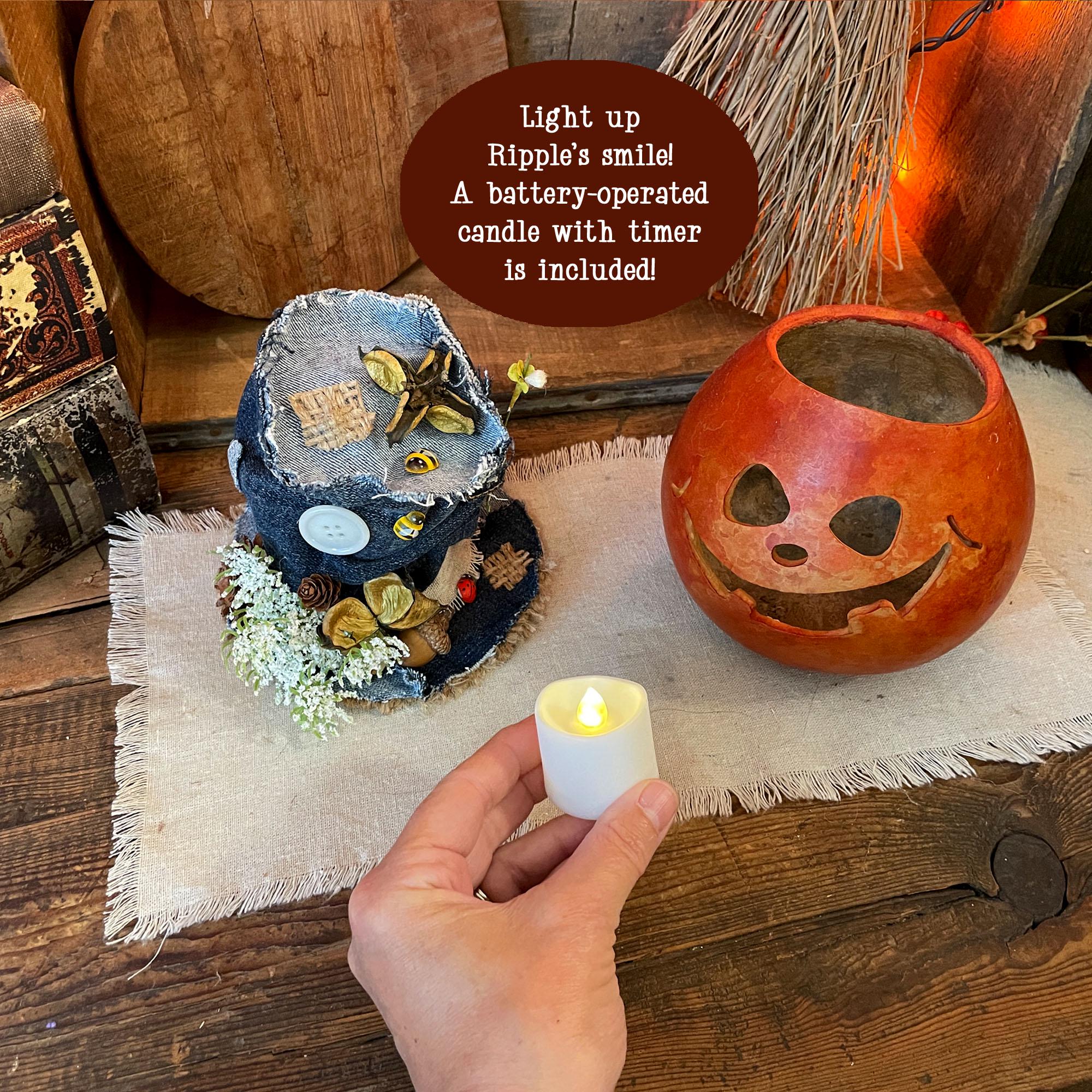 Decorative Halloween scene with a hand holding a battery-operated candle, surrounded by pumpkins and a broom.