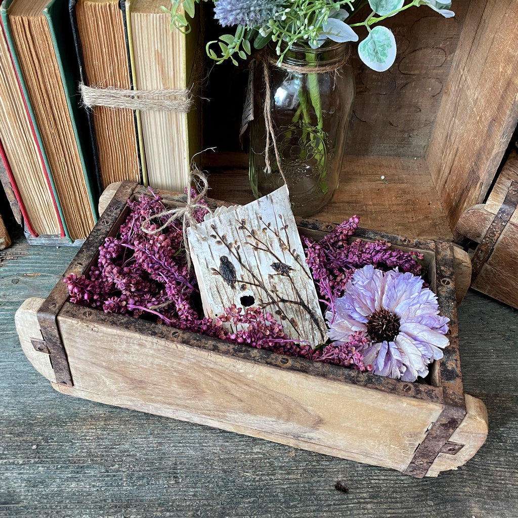 Wooden box with flowers and a jar of plants on a wooden surface
