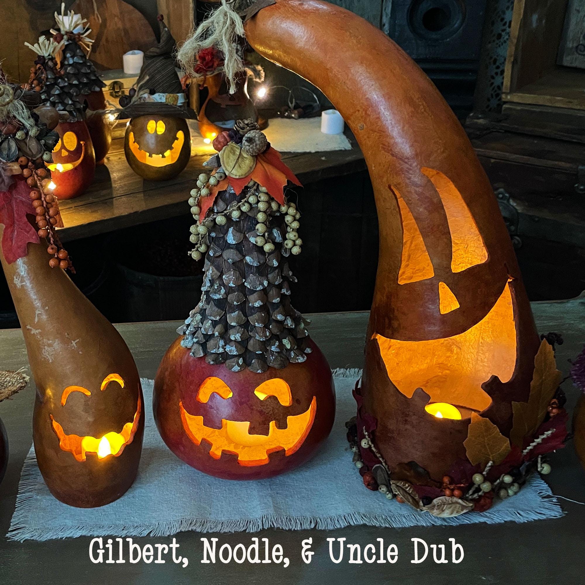 Three carved pumpkins with glowing lights on a table, decorated with pinecones and leaves.