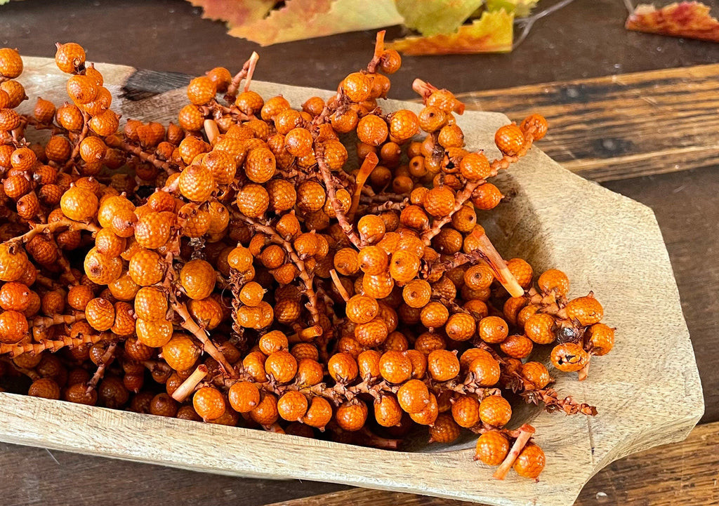 Dried orange berries on stems in a wooden bowl on a wooden surface with a rustic background.