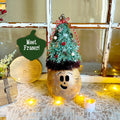 Decorative Christmas tree with a face on a table with candles and a window in the background.