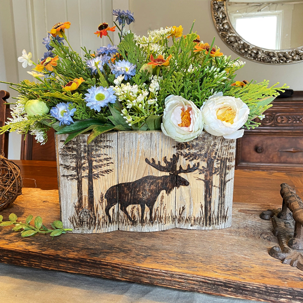 wood box centerpiece Floral arrangement in a wooden pot with moose design on a wooden surface