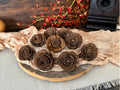 Decorative arrangement of brown pine cones shaped like flowers on a wooden board with a beige cloth underneath.