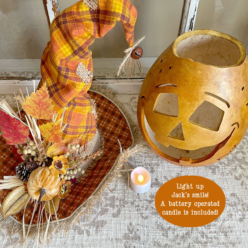 Decorative pumpkin lantern with a plaid hat and candle, surrounded by autumn-themed elements.