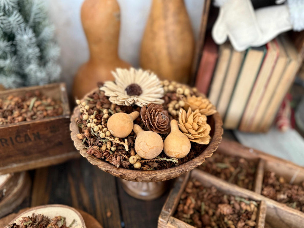 Decorative arrangement of dried flowers and gourds on a wooden stand with a rustic background.