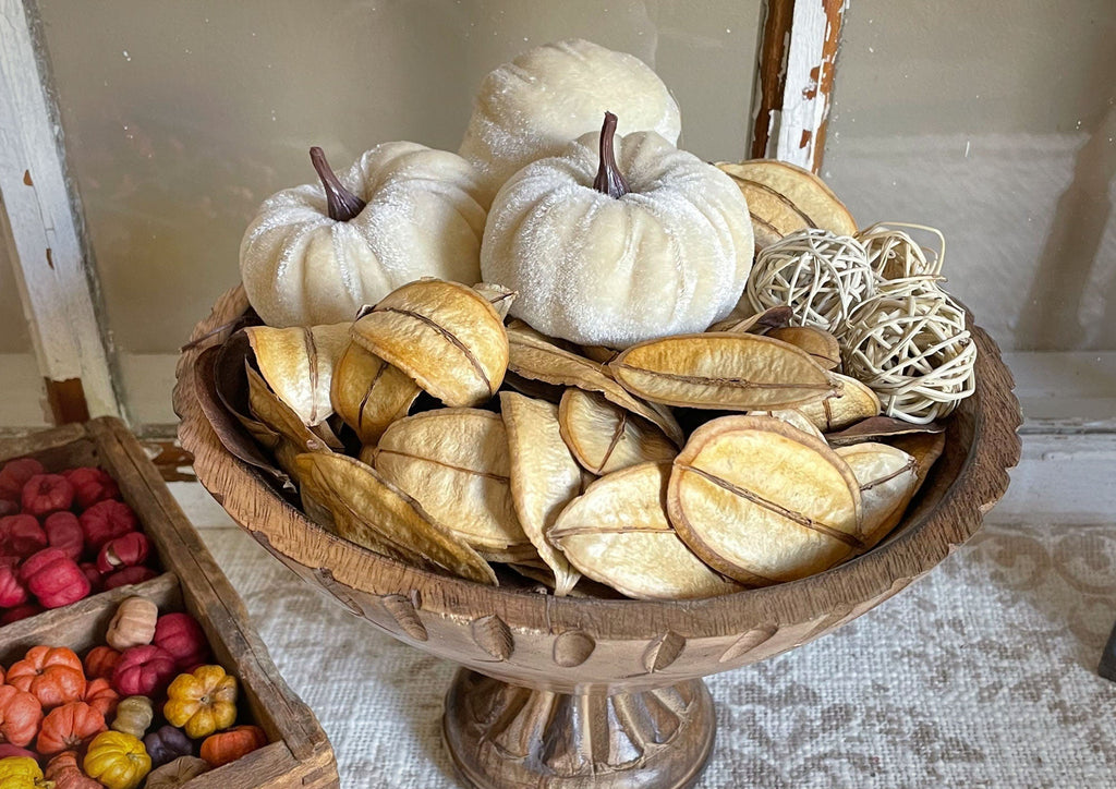 Decorative display with white pumpkins, dried leaves, and decorative balls in a wooden bowl.