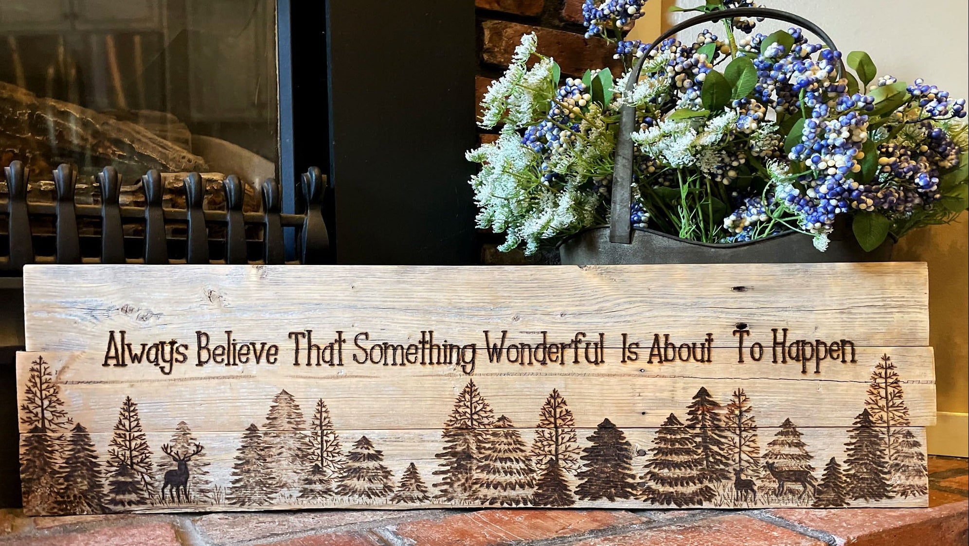 Wooden sign with nature design and text on a brick surface, with flowers in the background.