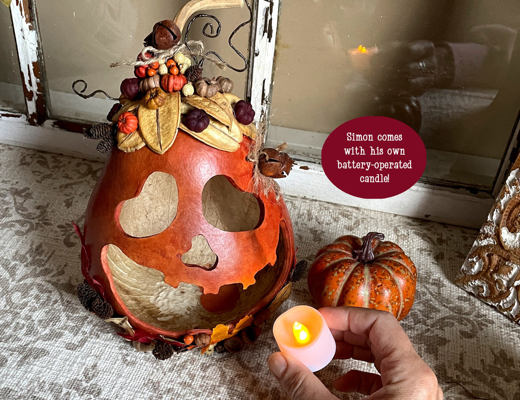 Decorative pumpkin with a battery-operated candle held by a hand, placed on a textured surface.