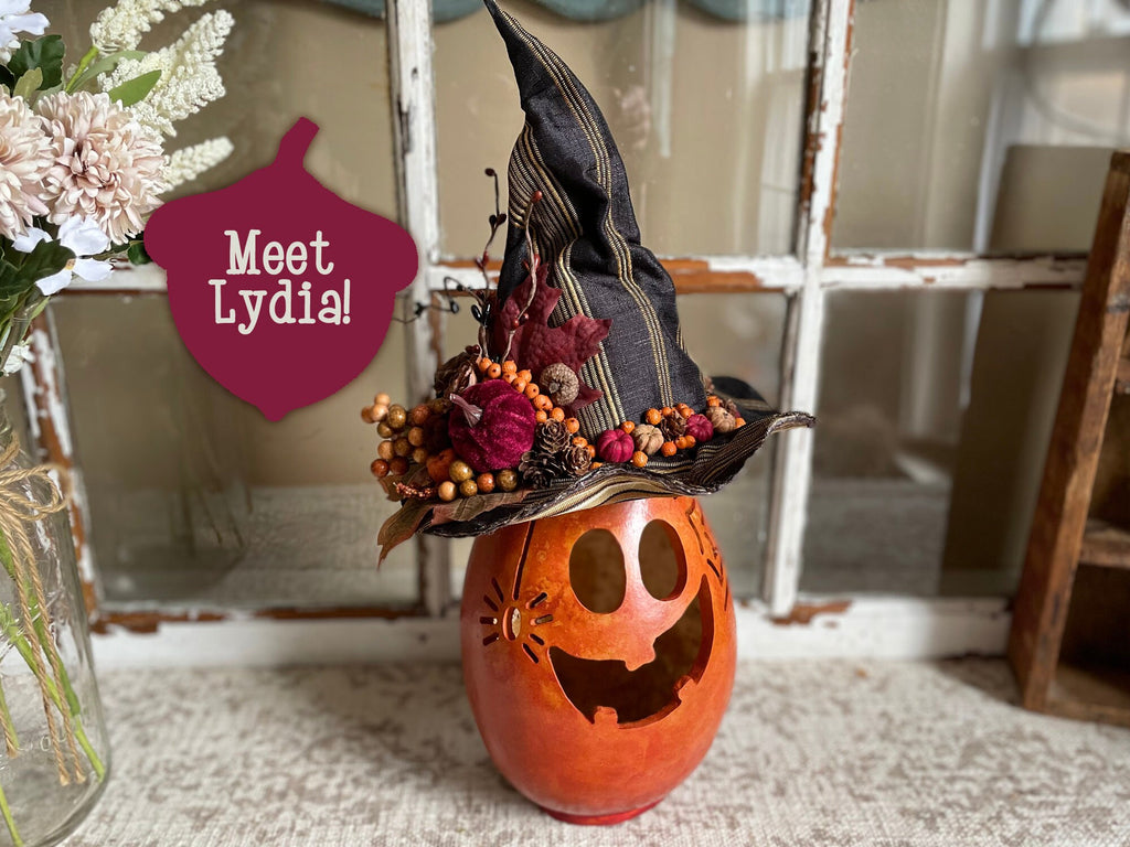 Decorative pumpkin with a witch hat and floral decorations, featuring a sign that says 'Meet Lydia'.