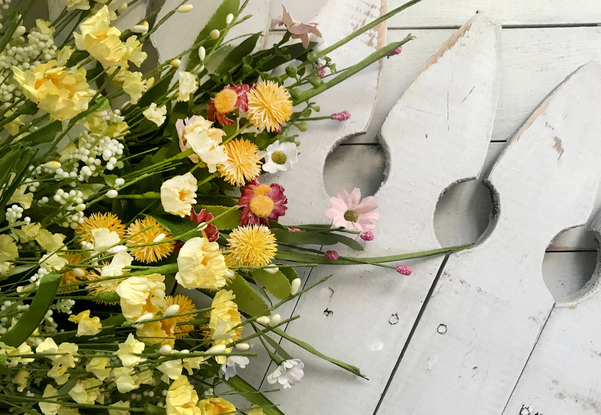 Bouquet of yellow and pink flowers on a white wooden surface with a decorative metal object.