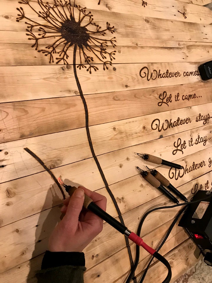 Hand plugging a cable into an electrical outlet on a wooden surface with engraved text.