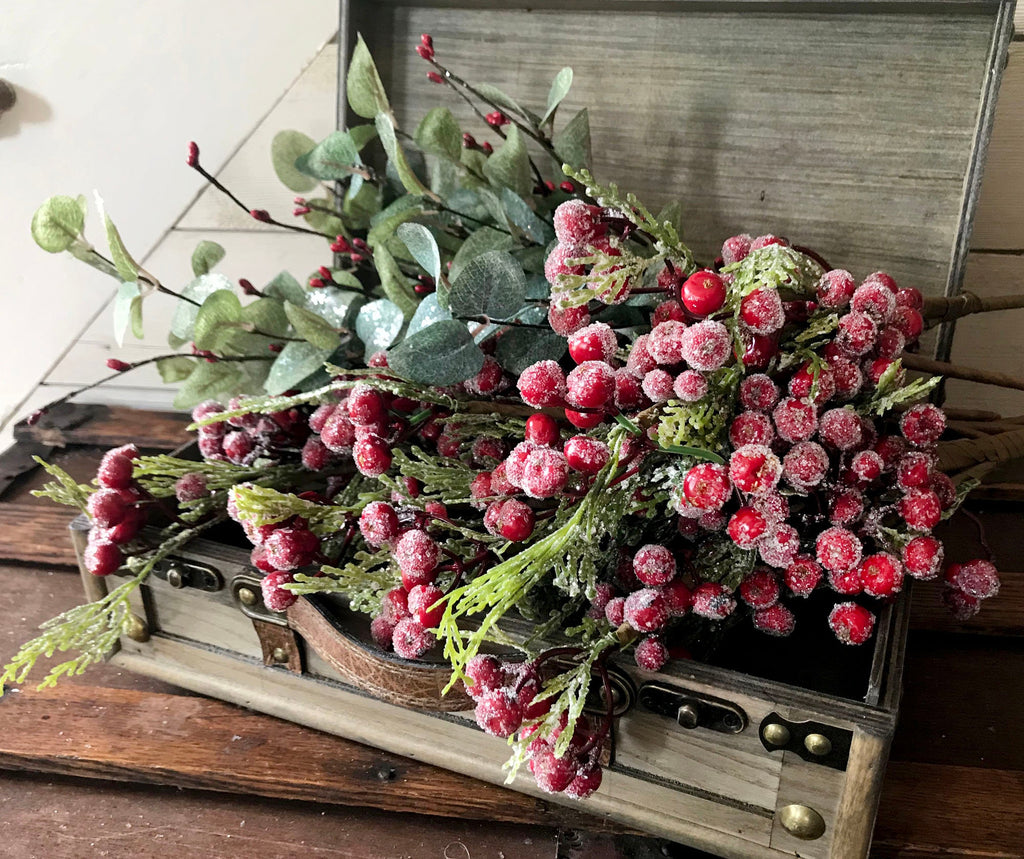 Decorative arrangement of red berries and greenery in an old wooden suitcase.