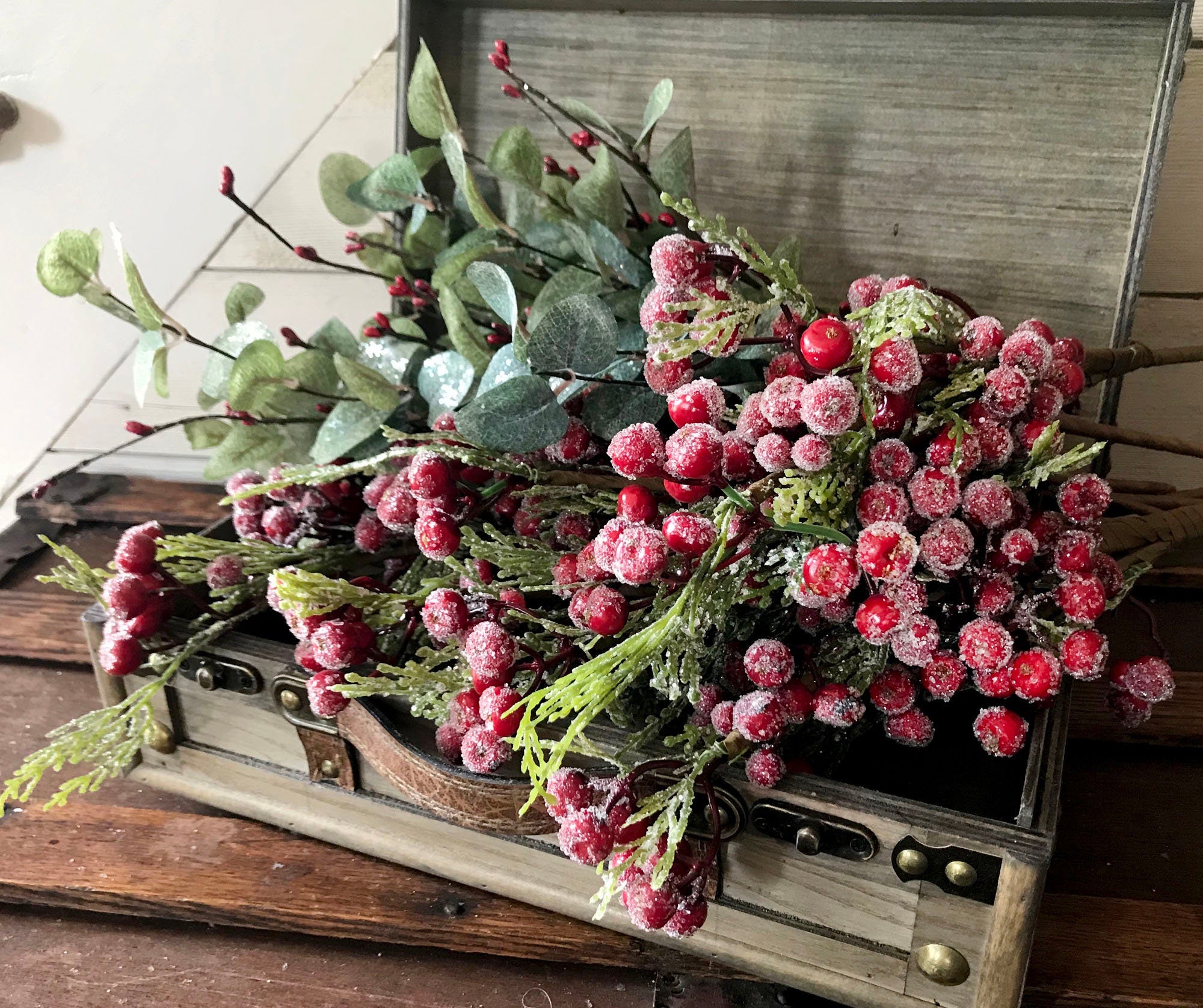 Decorative arrangement of red berries and greenery in an old wooden suitcase.
