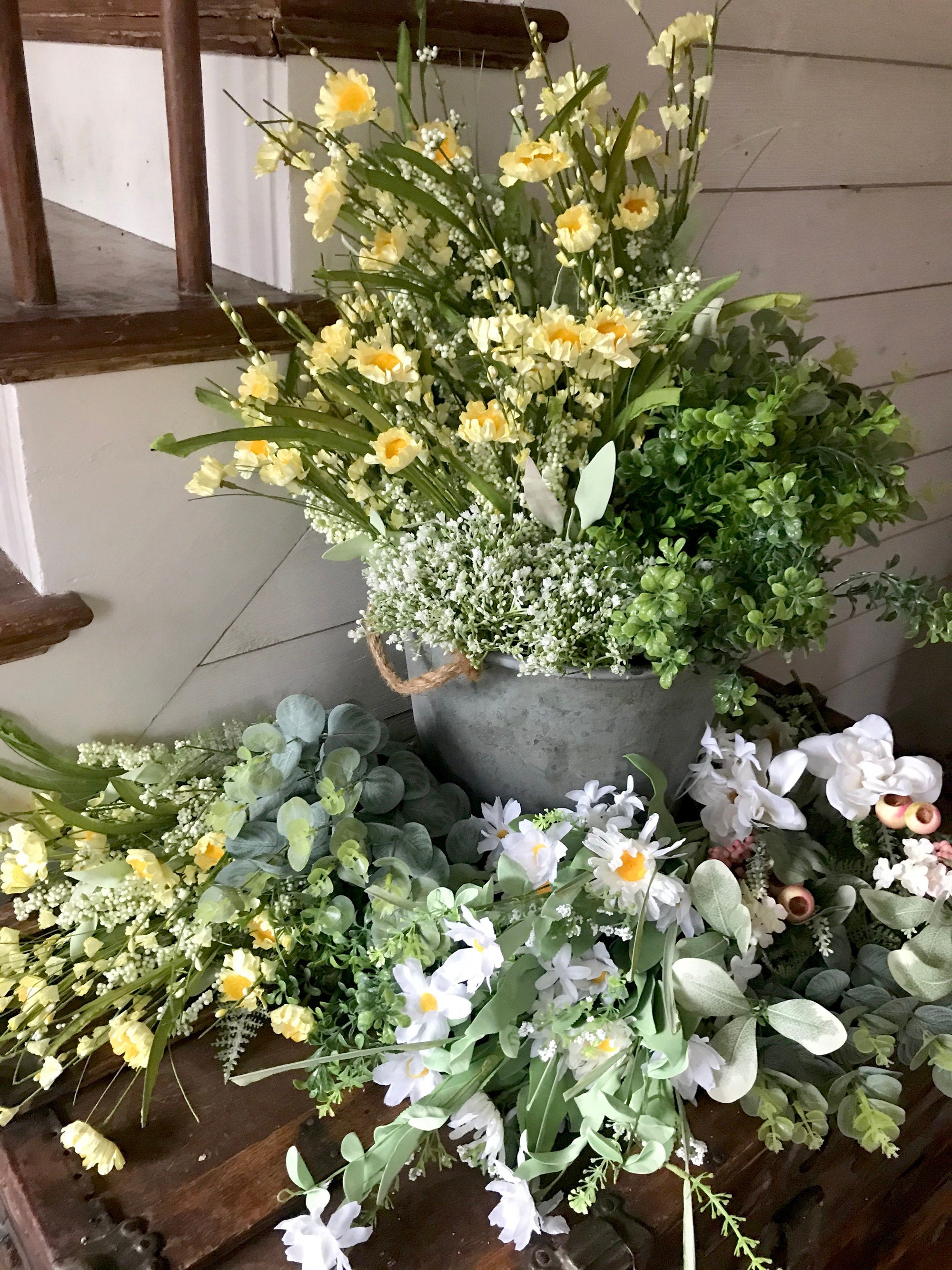 Collection of potted plants and flowers on a wooden surface with a white wall background.