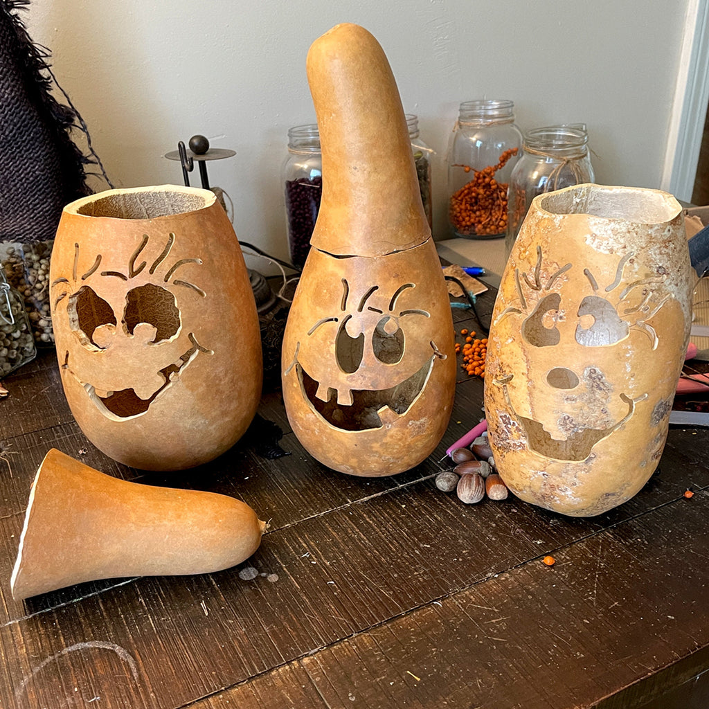 Three carved gourds with Halloween designs on a wooden surface.