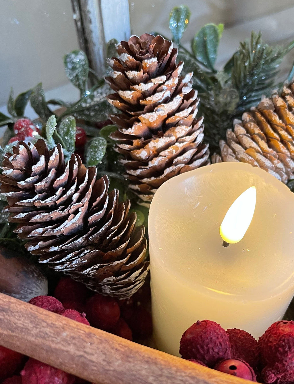 Decorative arrangement with pine cones, berries, and a candle on a white background.
