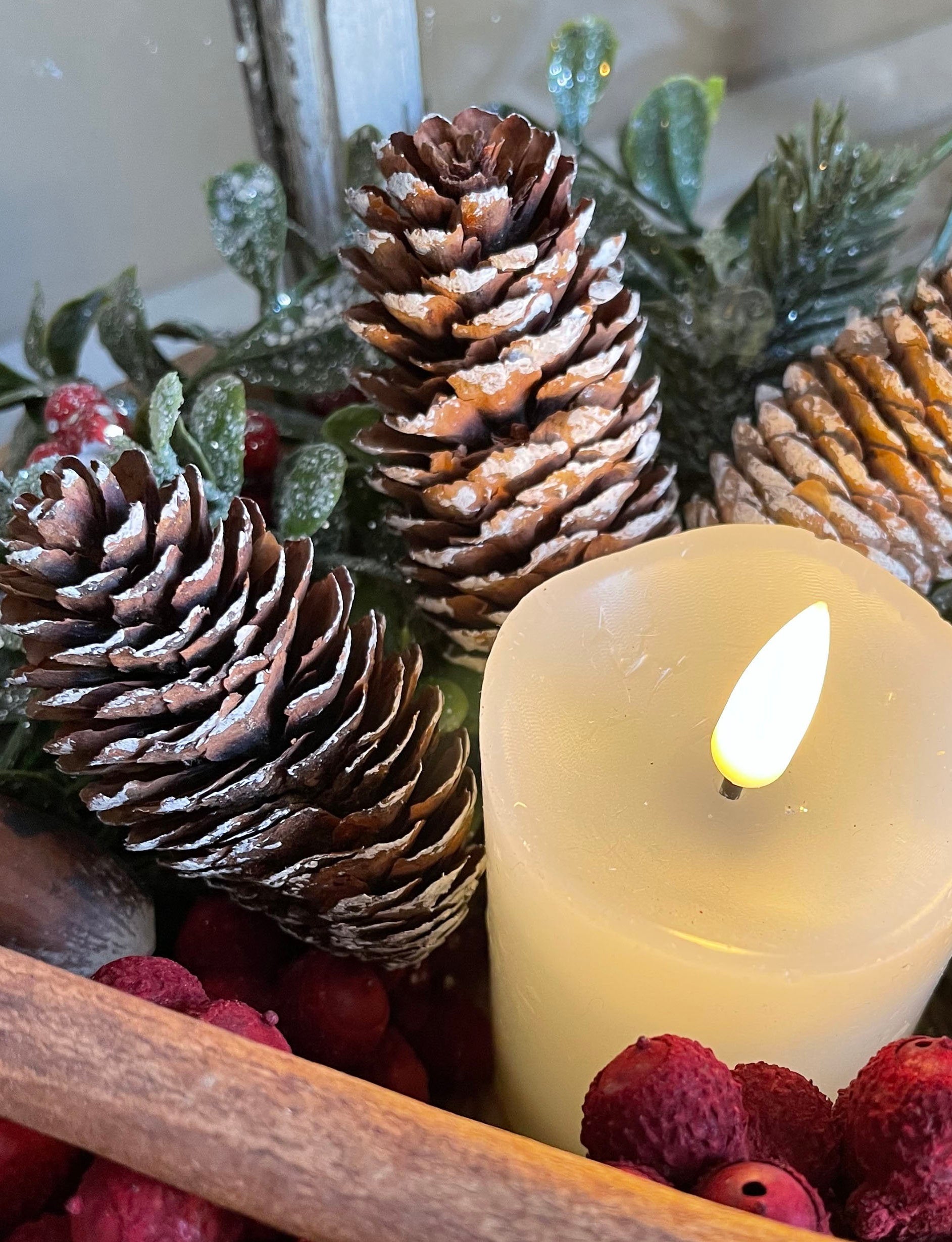 Decorative arrangement with pine cones, berries, and a candle on a white background.