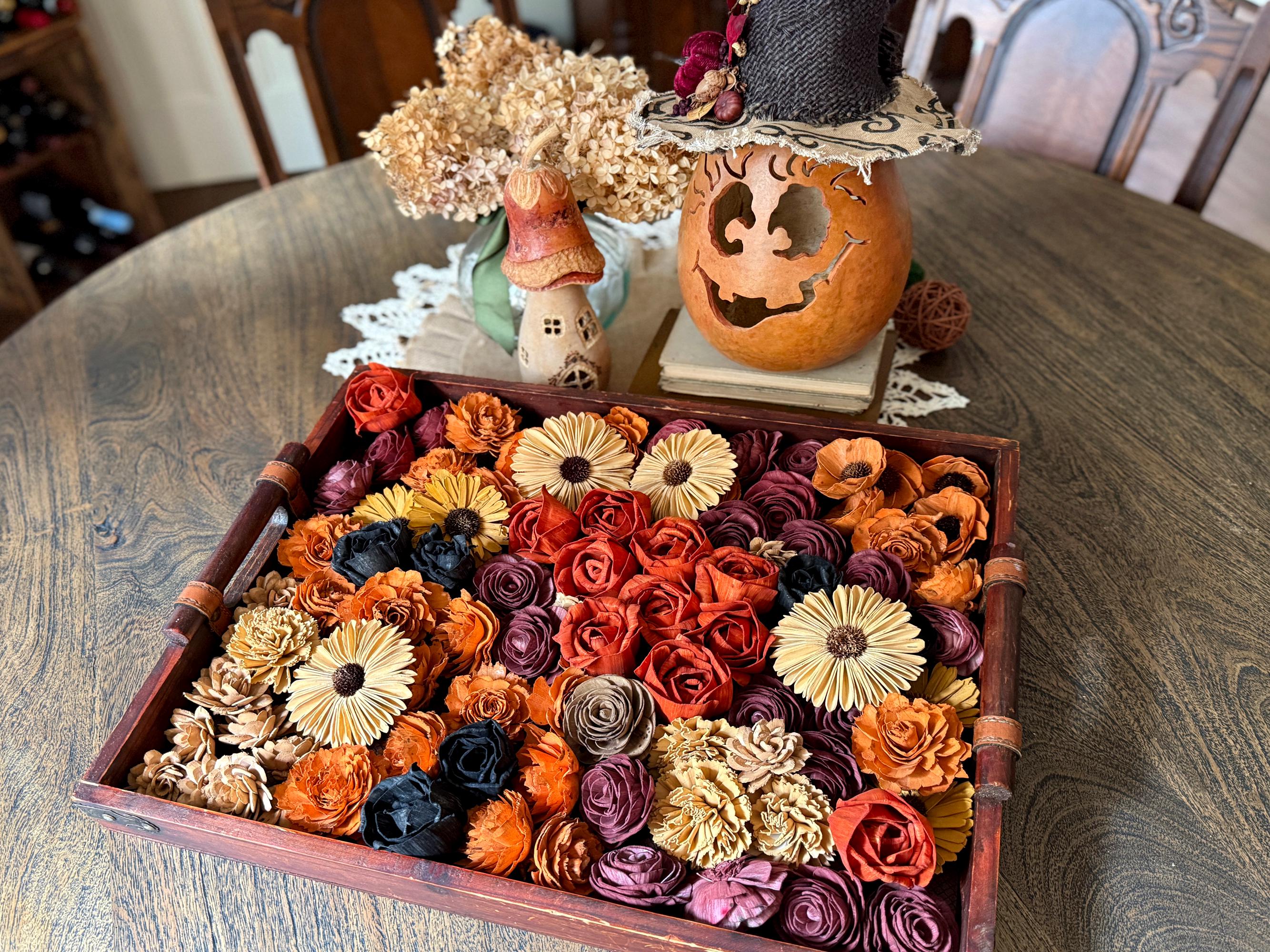 Decorative tray with assorted flowers, pumpkin, and small house on a wooden table.