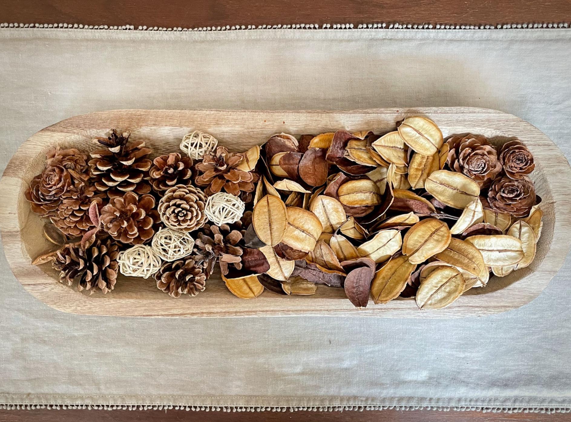 Wooden dough bowl with assorted dried flowers and pine cones on a neutral background on a coffee table runner