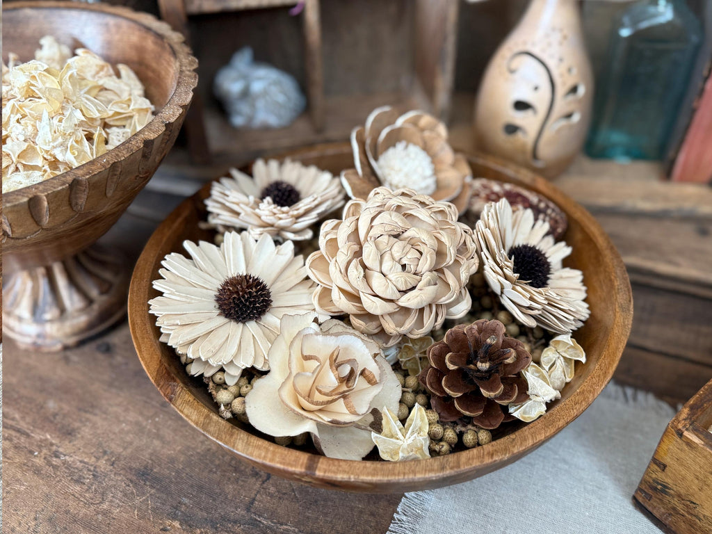 Wooden bowl with decorative flowers and pinecones on a rustic wooden surface.