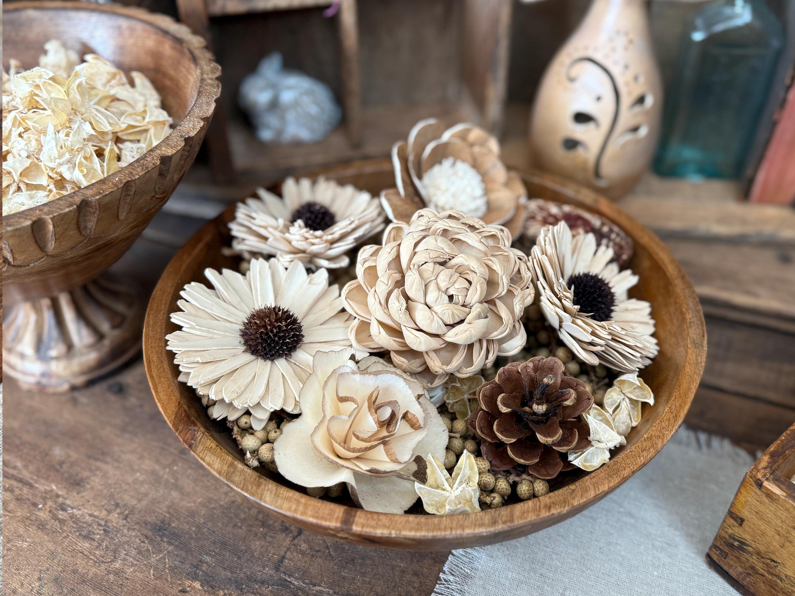 Wooden bowl with decorative flowers and pinecones on a rustic wooden surface.