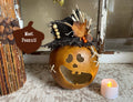 Decorative pumpkin with a face and autumnal decorations on a textured surface with a candle.
