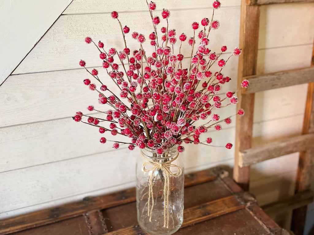Vase with red berries on a wooden surface against a white paneled wall