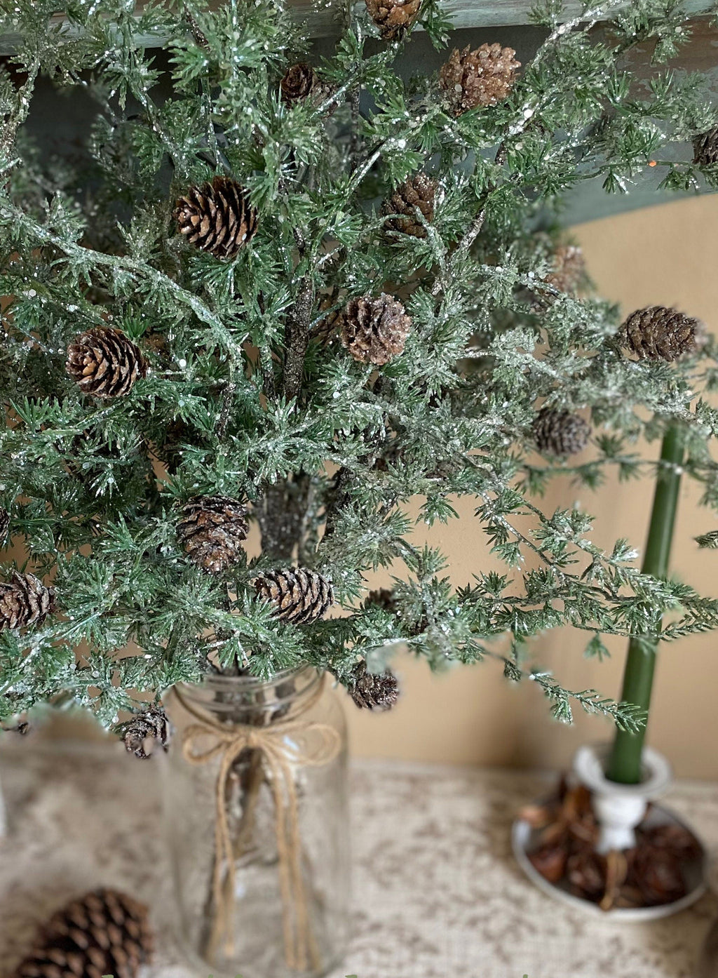 Decorative Christmas tree with pinecones in a glass vase on a textured surface.