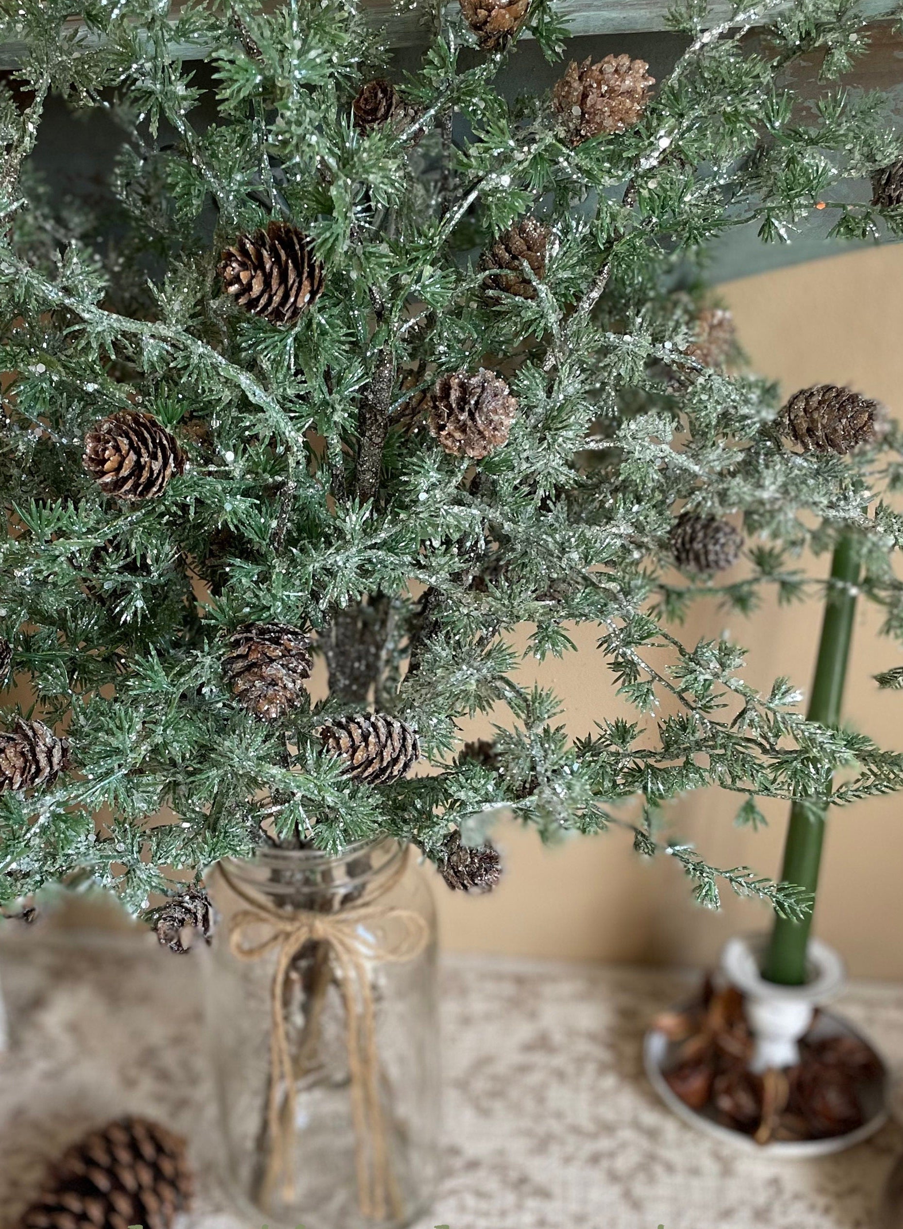 Decorative Christmas tree with pinecones in a glass vase on a textured surface.