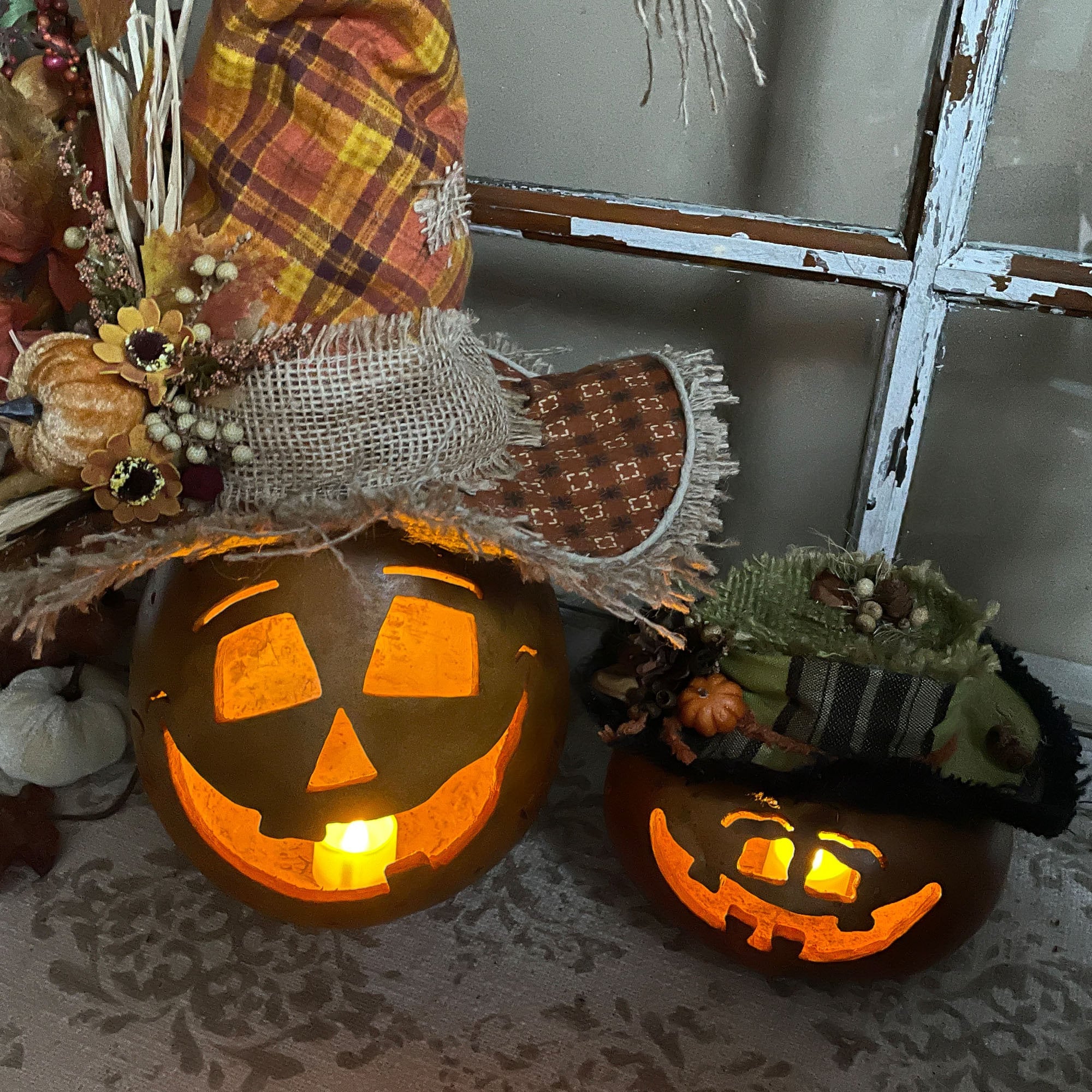 Two lit jack-o'-lanterns on a textured surface with decorative elements in the background.