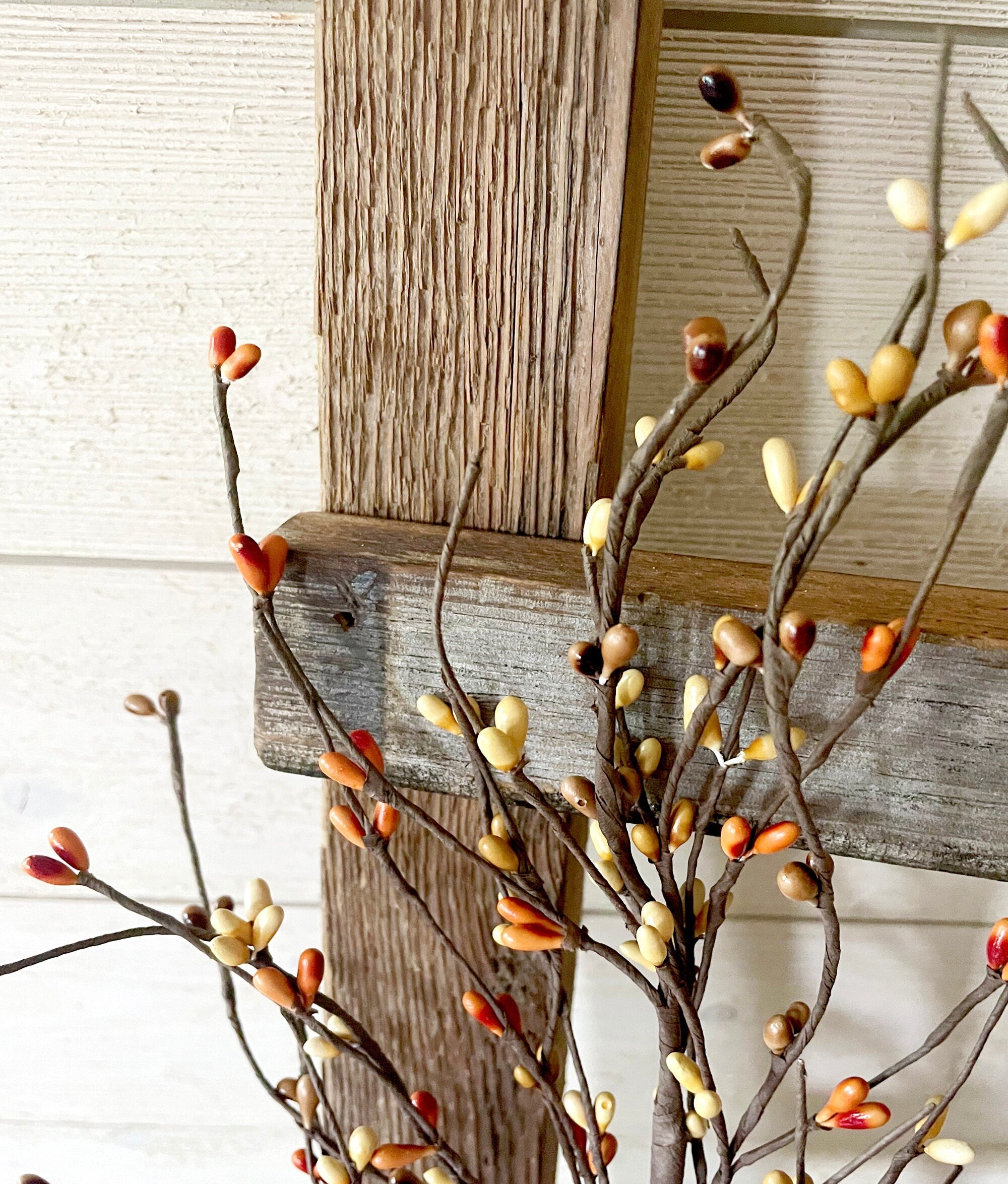 Decorative branches with berries against a wooden ladder against a white wall.