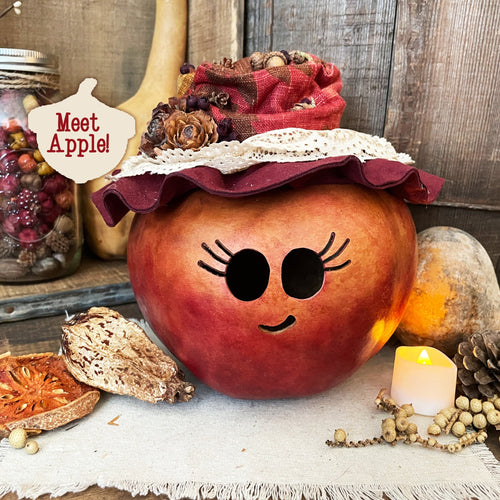 Decorative pumpkin with a face, wearing a red hat, on a rustic background with candles and pinecones.