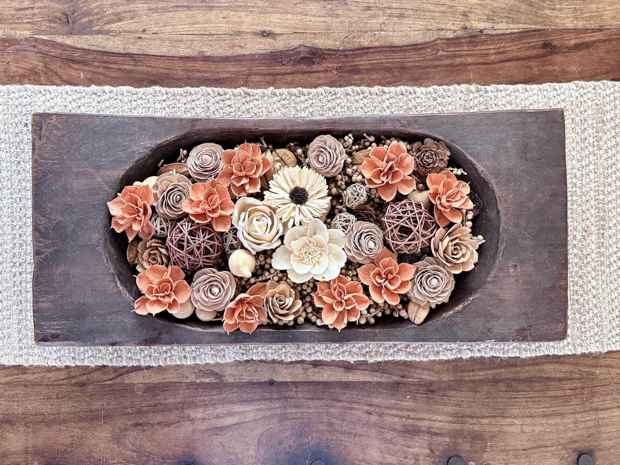Decorative floral arrangement in a large wooden dough bowl on a coffee table. Flowers are orange and beige