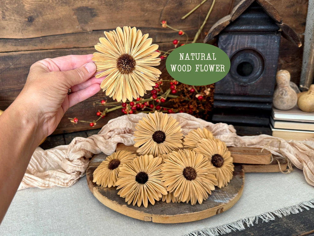 Hand holding a natural wood flower with more flowers on a wooden board, rustic background.