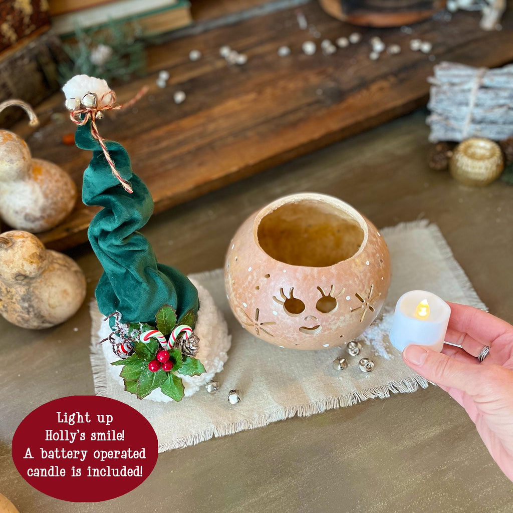 Decorative lantern with a face, surrounded by pumpkins and a small candle, on a wooden surface.