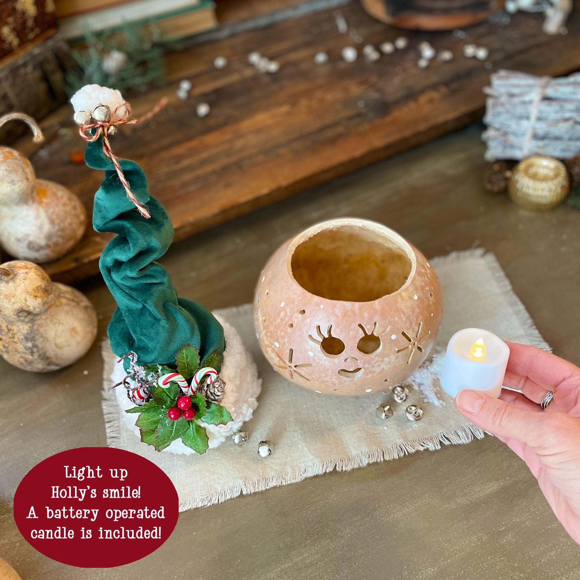 Decorative lantern with a face, surrounded by pumpkins and a small candle, on a wooden surface.
